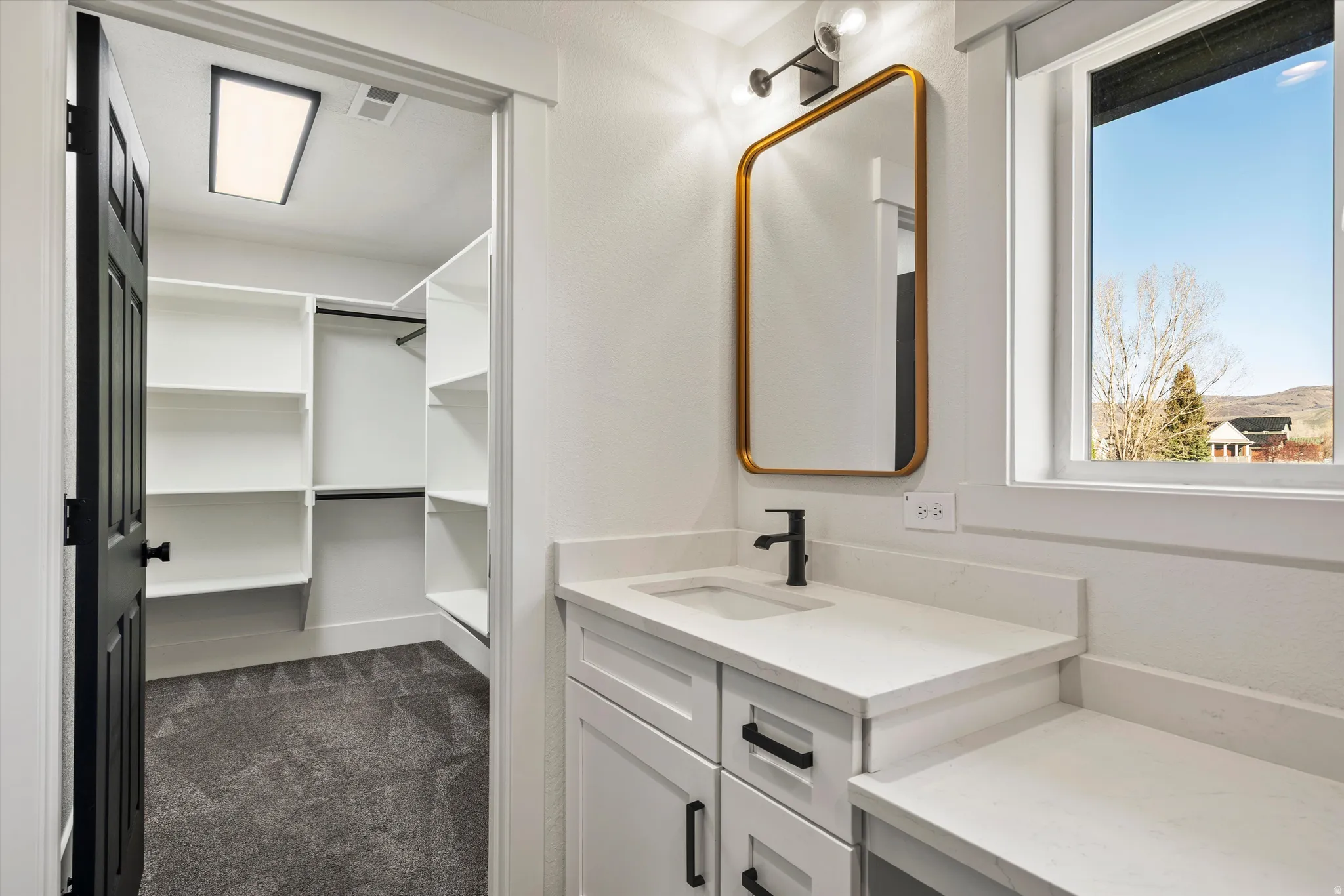 Bathroom with vanity, dark colored carpet, and a walk in closet