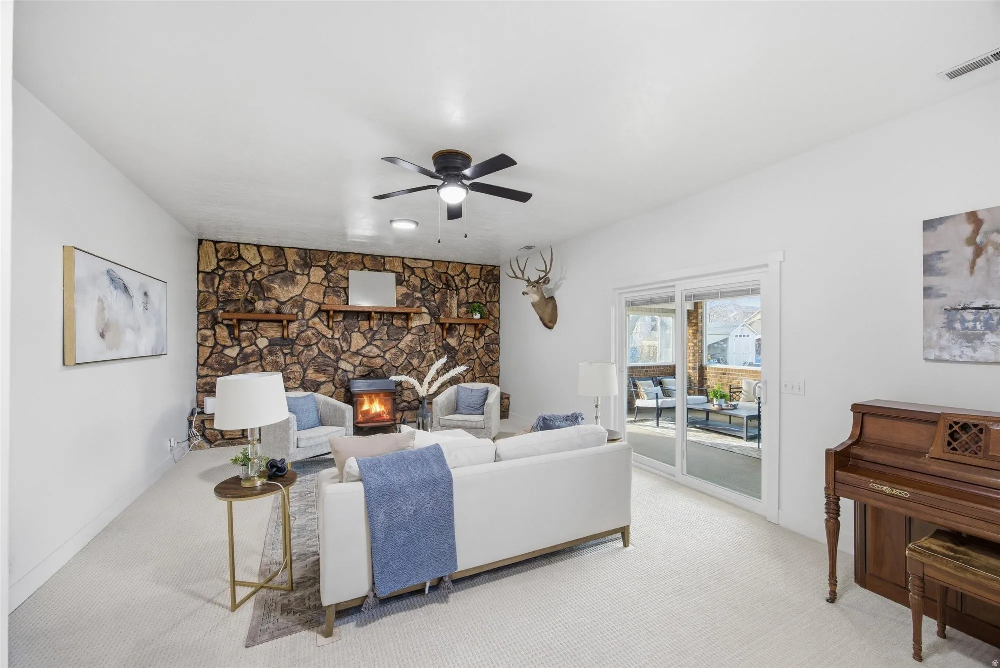 Living room featuring ceiling fan, light carpet, and a wood burning stove