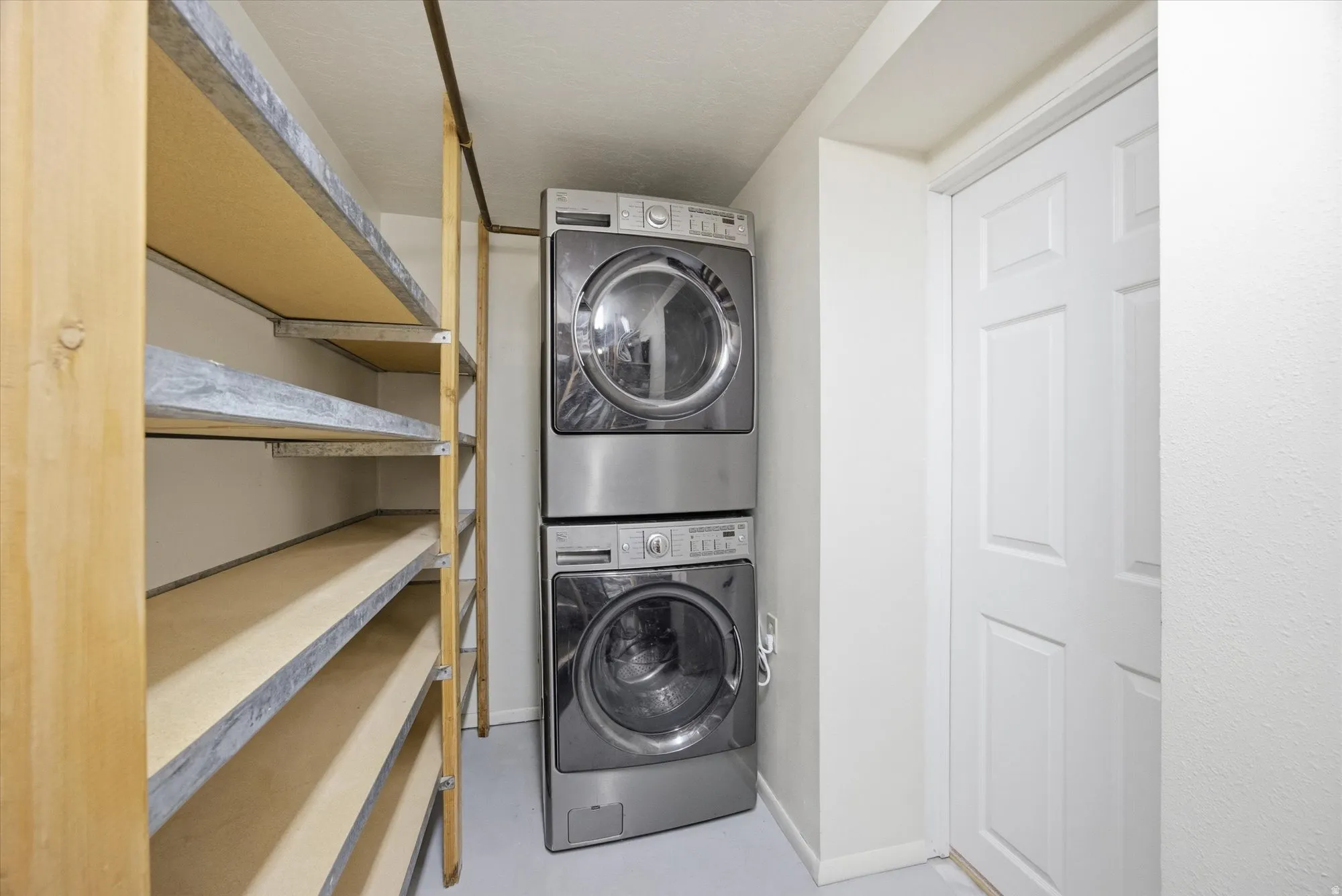 Laundry area with stacked washer and clothes dryer and concrete floors