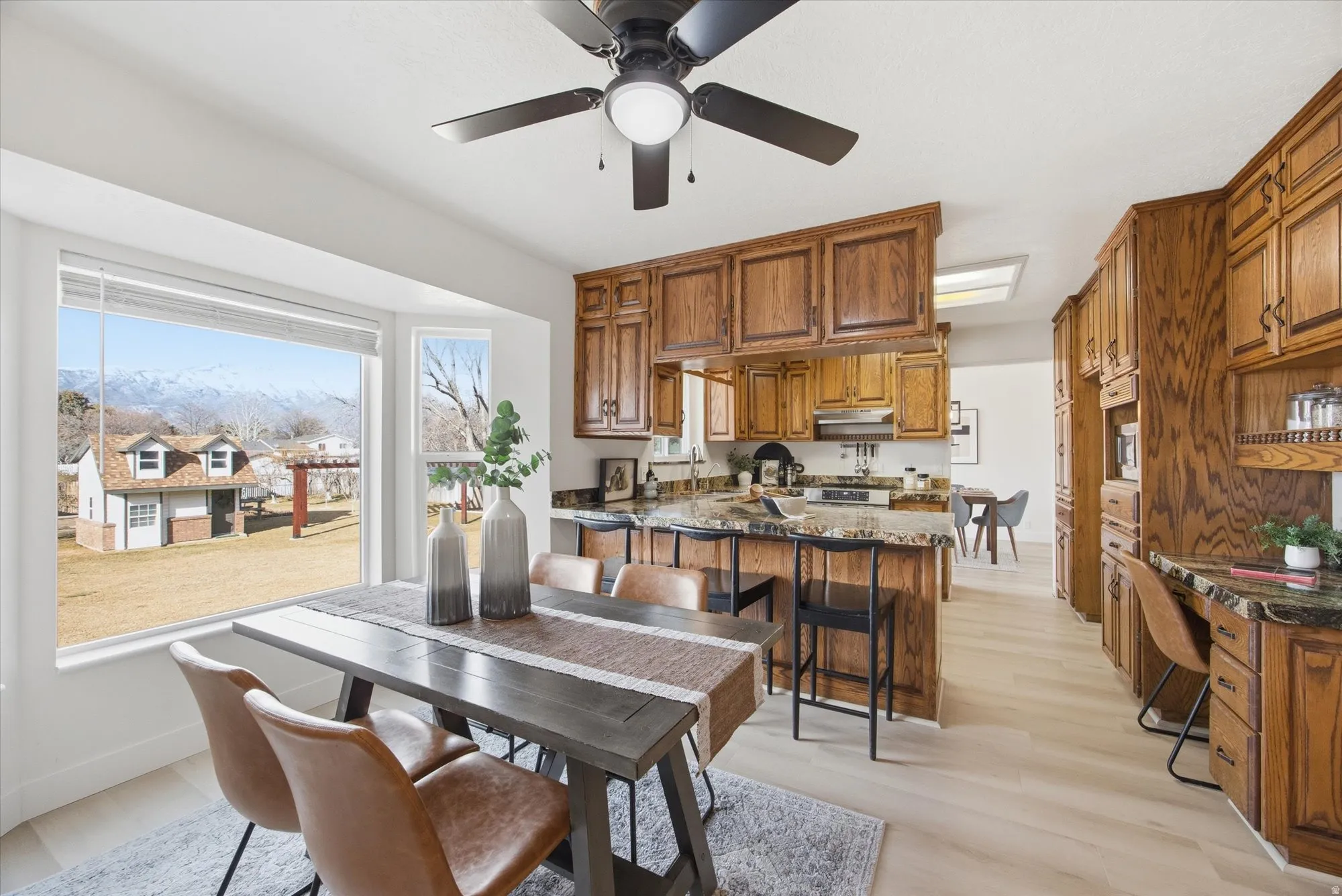 Kitchen with a peninsula, stainless steel electric stove, ceiling fan, oak cabinets, LVP flooring and dark stone counters