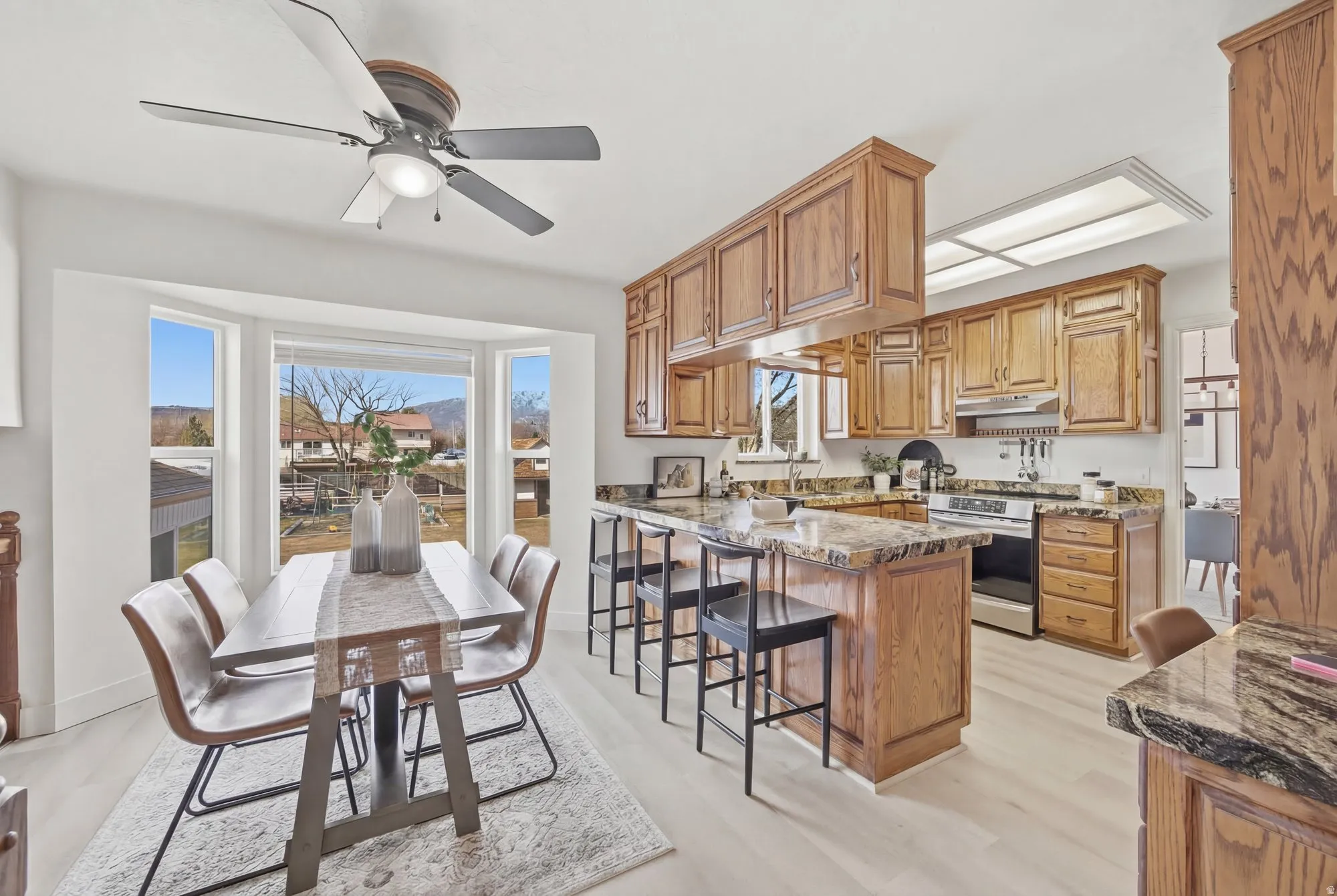 Kitchen with a peninsula, stainless steel electric stove, ceiling fan, oak cabinets, LVP flooring and dark stone counters