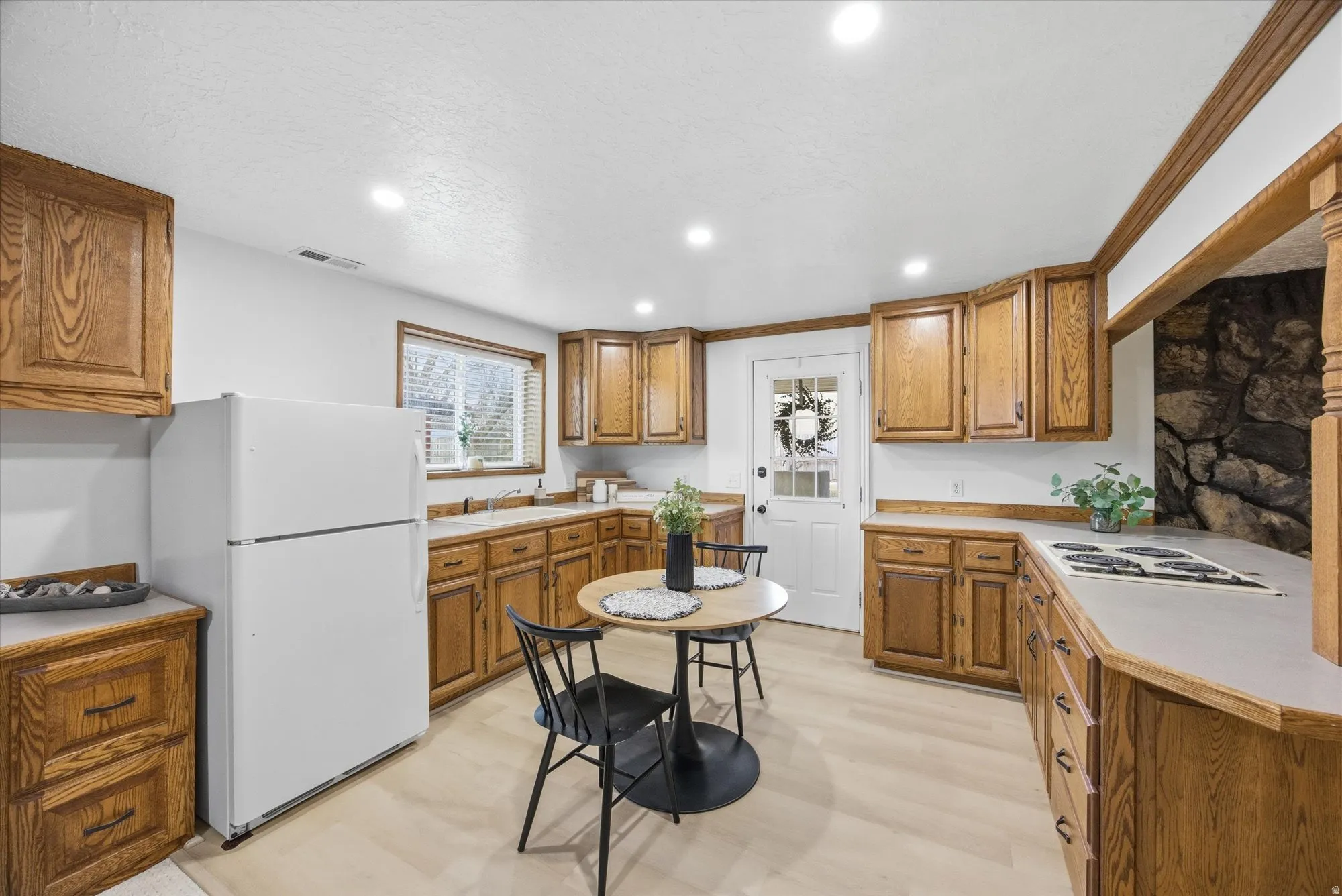 Kitchen featuring wood finish cabinets, light countertops, white appliances, recessed lighting, and light wood finished floors