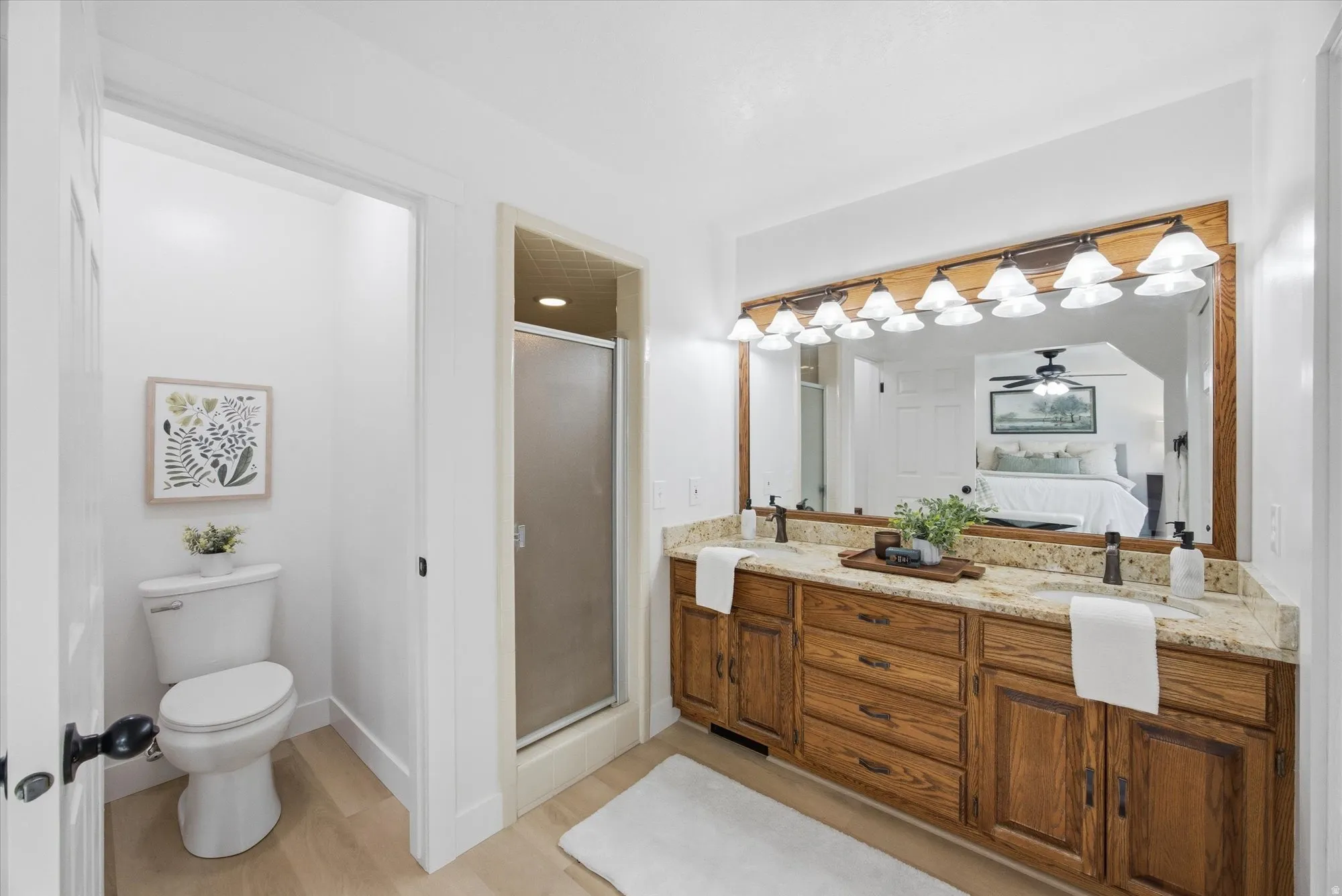 Full bath with a stall shower, connected bathroom, double vanity, and light LVP flooring