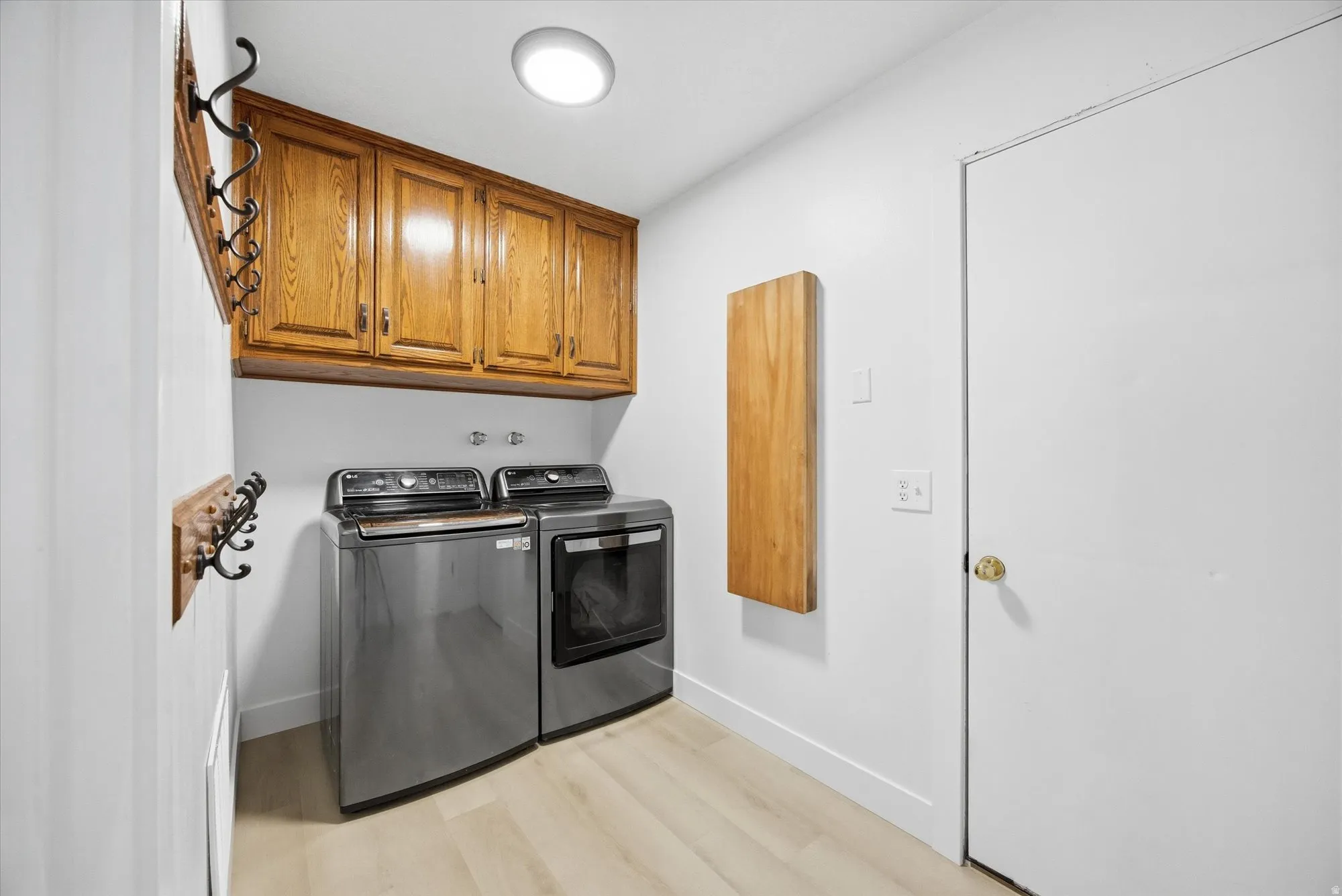 Laundry area featuring light LVP flooring, washing machine and clothes dryer, and cabinet space