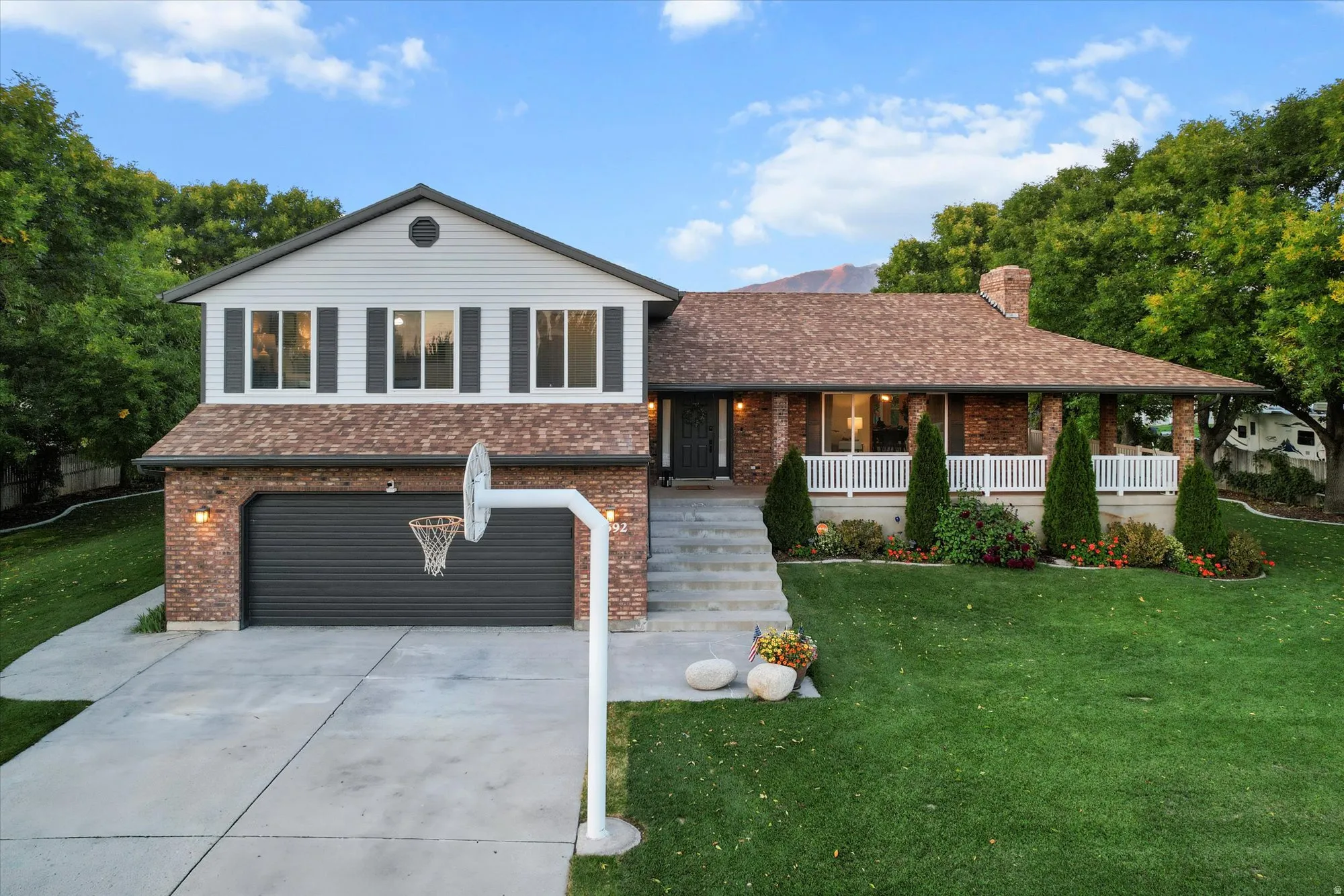Tri-level home featuring driveway, brick siding, a garage, a front lawn, and covered porch