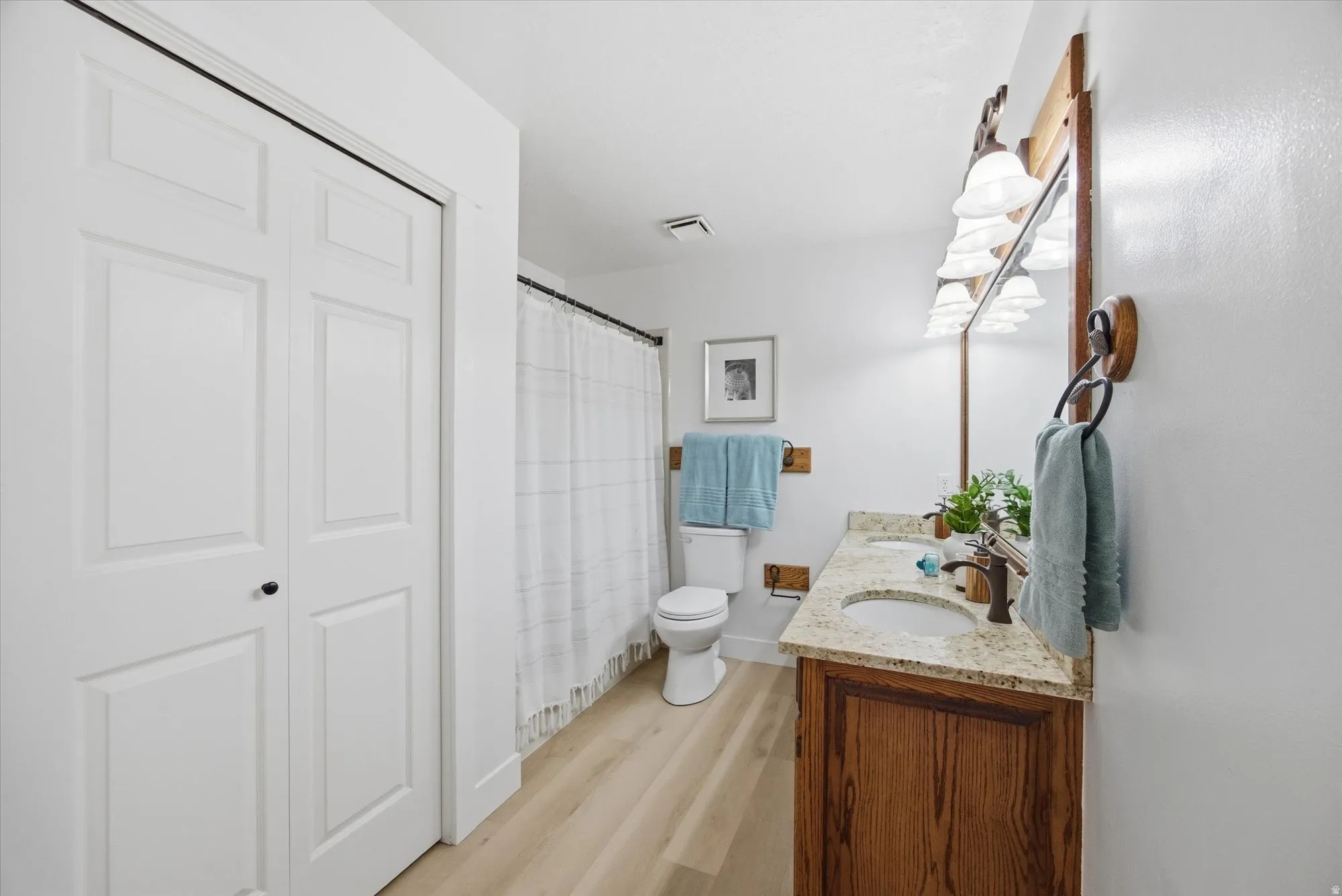 Full bath featuring double vanity, a shower with curtain, and light LVP flooring