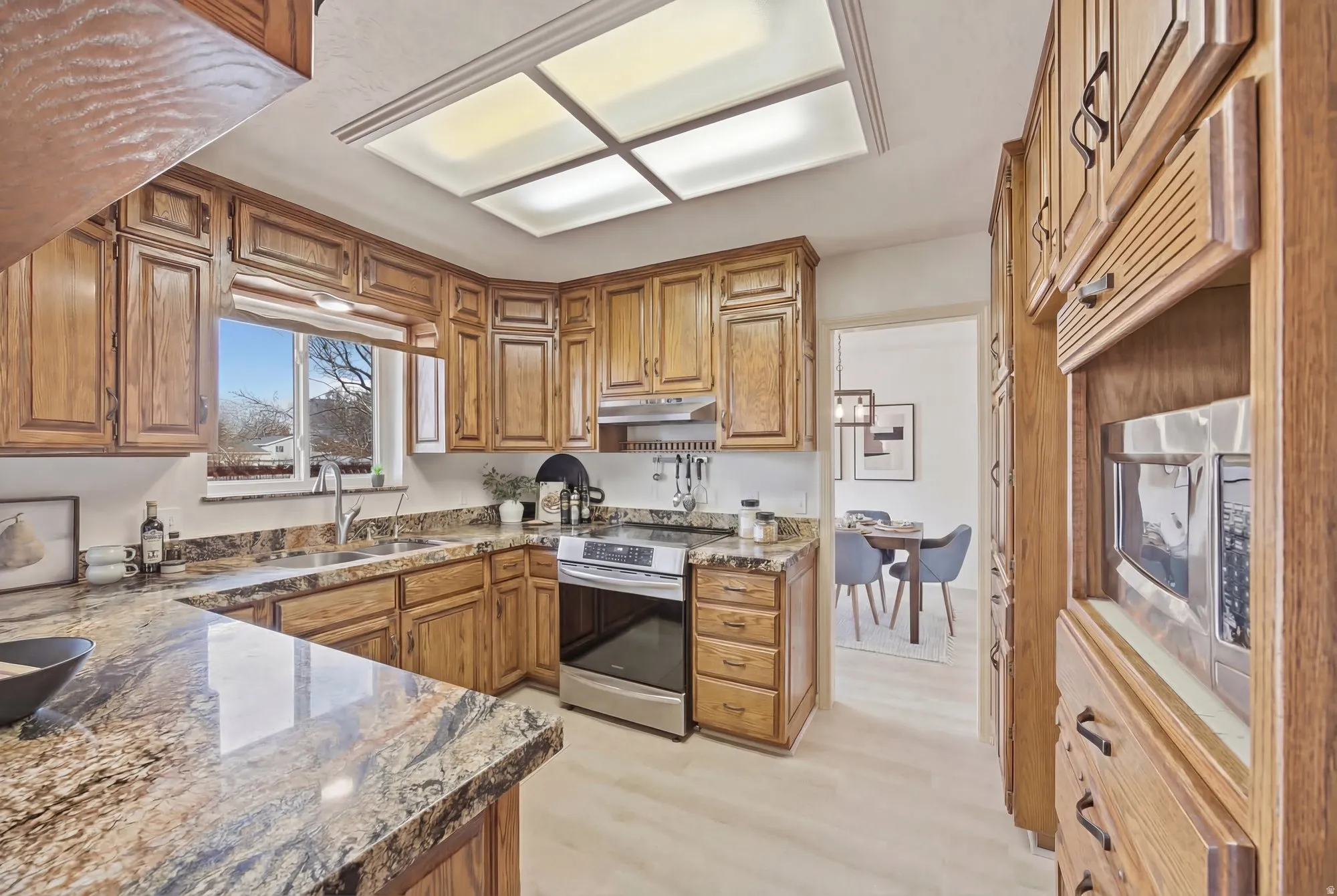 Kitchen with wood finish cabinets, stainless steel appliances, dark stone countertops, and light wood-style floors