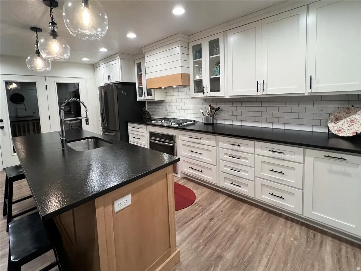 Kitchen with a breakfast bar area, a center island with sink, glass fronted cabinets, light wood finished floors, and white cabinets