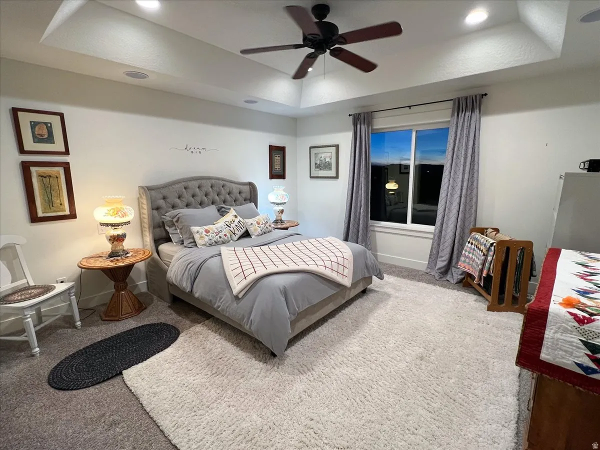 Carpeted bedroom featuring a raised ceiling, ceiling fan, and recessed lighting