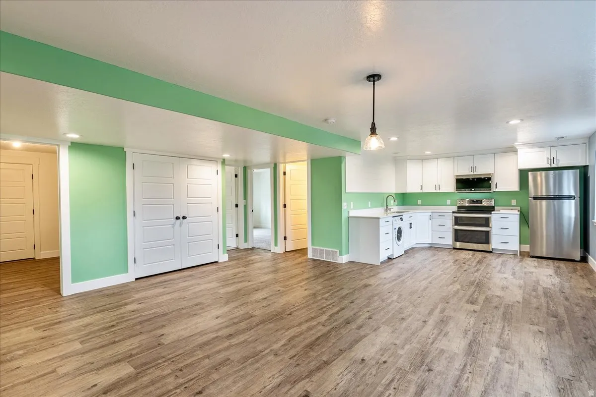 Kitchen with stainless steel appliances, light countertops, white cabinets, light wood-style floors, and pendant lighting