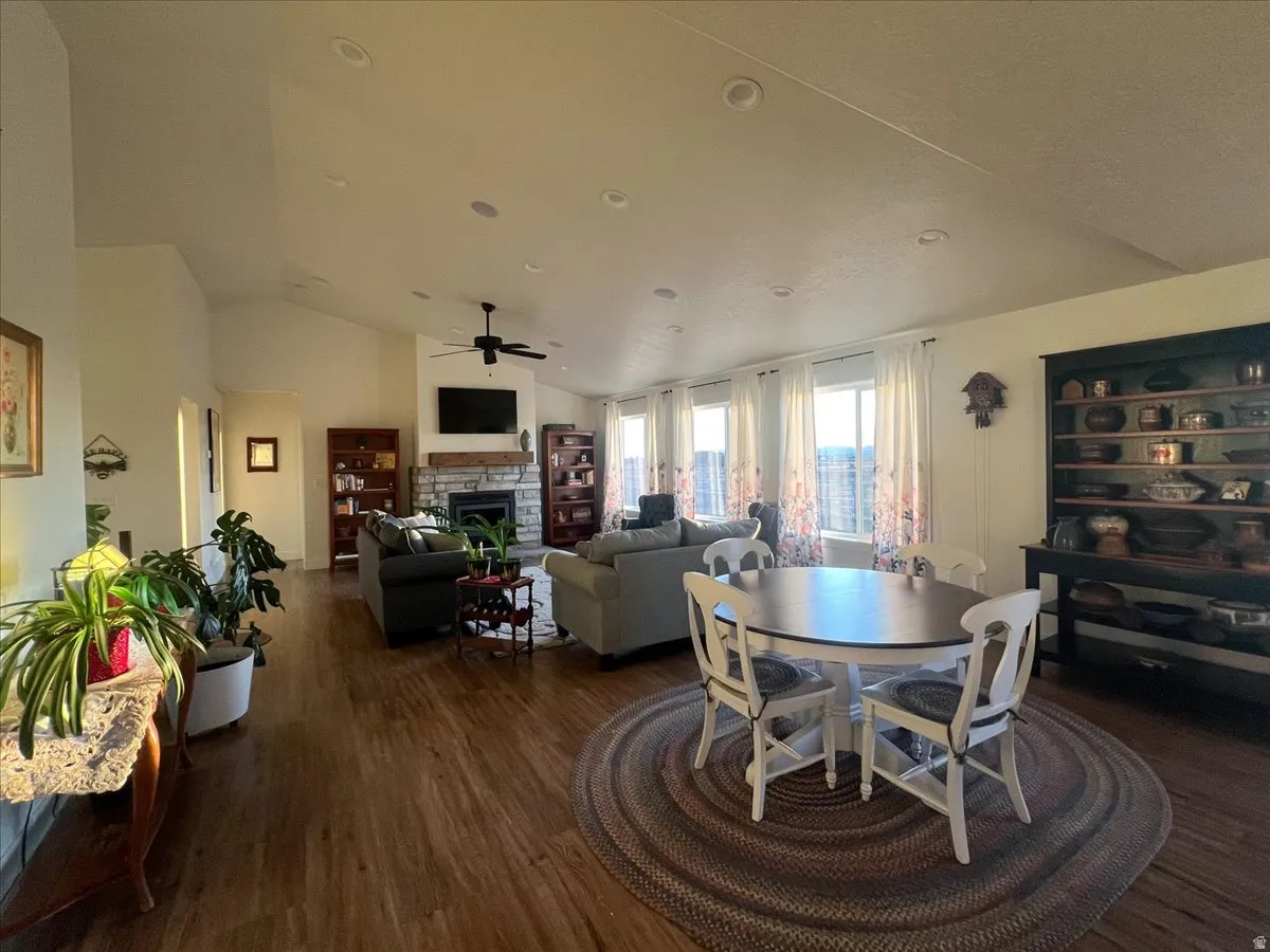 Dining room featuring lofted ceiling, dark wood-style flooring, a stone fireplace, and a ceiling fan