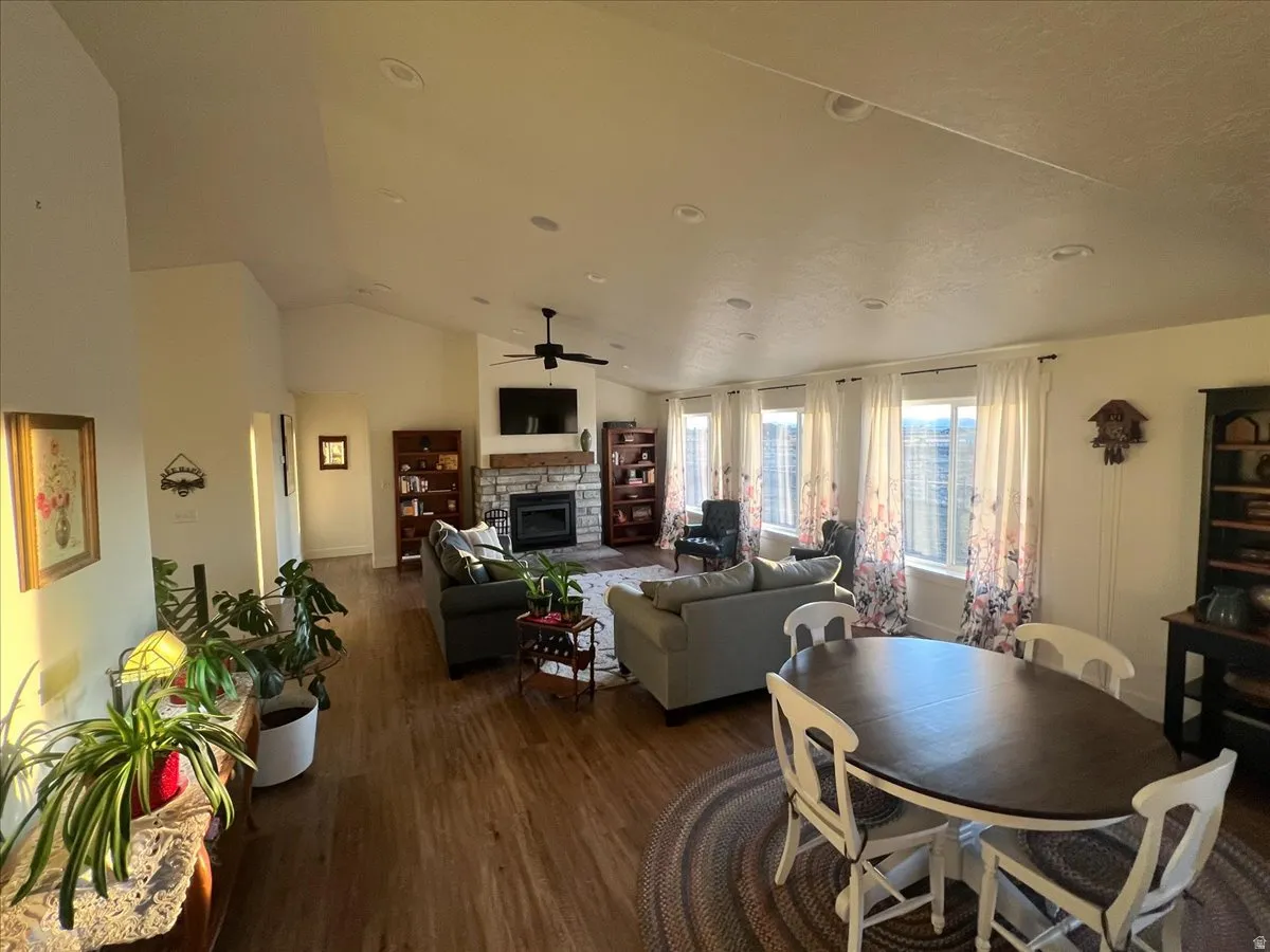 Dining room featuring dark wood-type flooring, lofted ceiling, a fireplace, and a ceiling fan