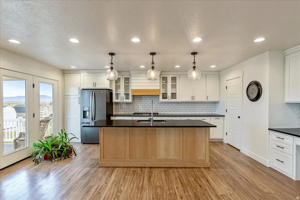 Kitchen with glass insert cabinets, stainless steel fridge, a center island with sink, a textured ceiling, and light wood finished floors