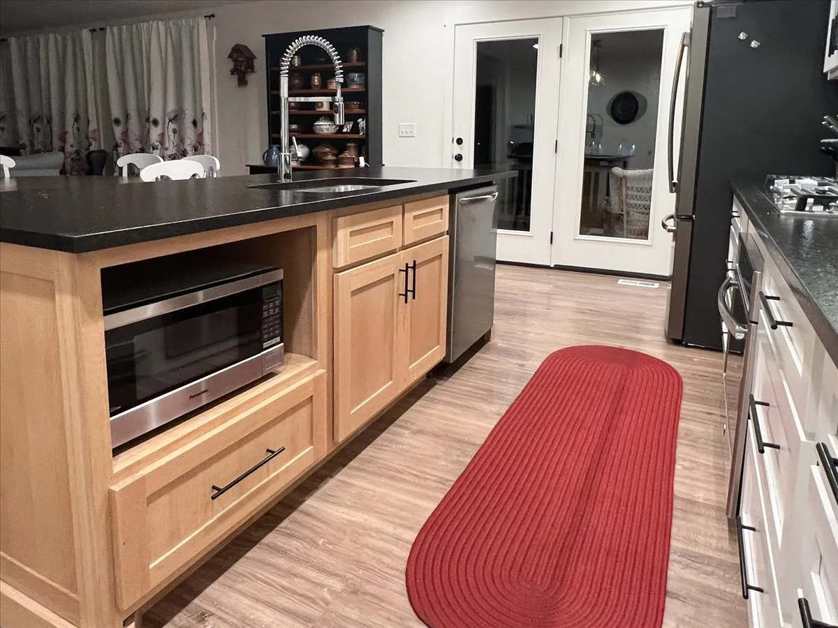 Kitchen with light wood finish cabinetry, stainless steel appliances, light wood-type flooring, and a kitchen island with sink