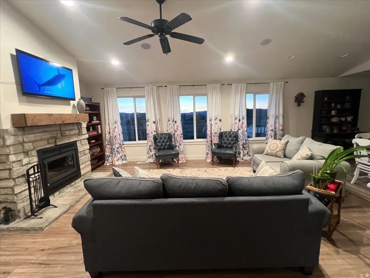 Living room featuring vaulted ceiling, light wood finished floors, a stone fireplace, a ceiling fan, and recessed lighting
