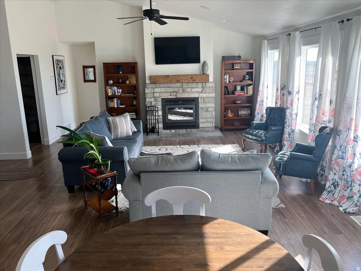 Living area featuring vaulted ceiling, a stone fireplace, dark wood-type flooring, and a ceiling fan
