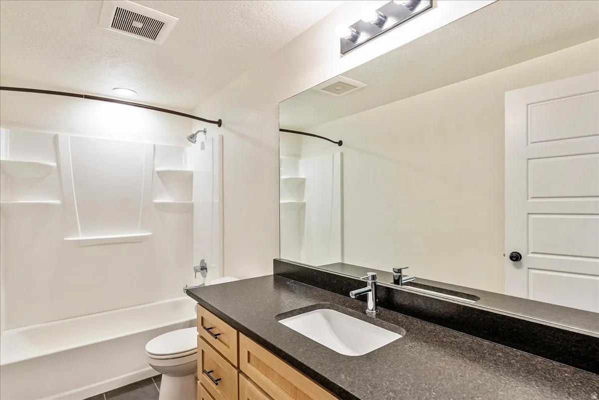 Bathroom featuring vanity, a textured ceiling, shower / tub combination, and dark tile patterned flooring
