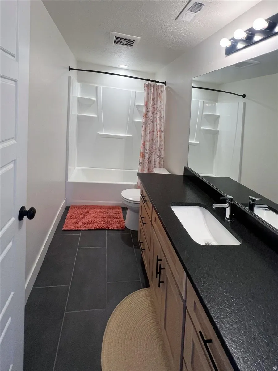 Full bath with vanity, a textured ceiling, shower / tub combo, and dark tile patterned flooring