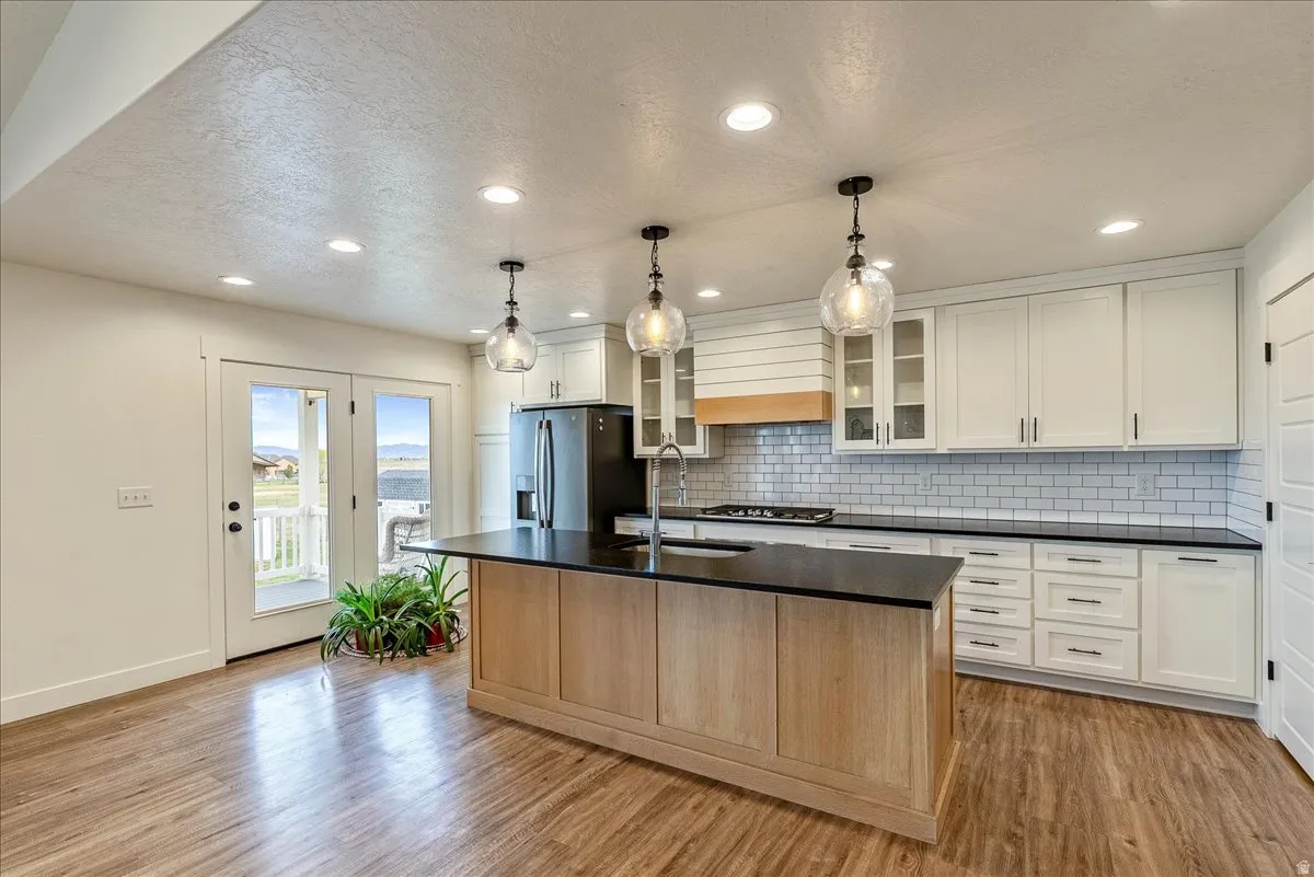 Kitchen featuring glass fronted cabinets, white cabinets, a kitchen island with sink, stainless steel appliances, and light wood-type flooring