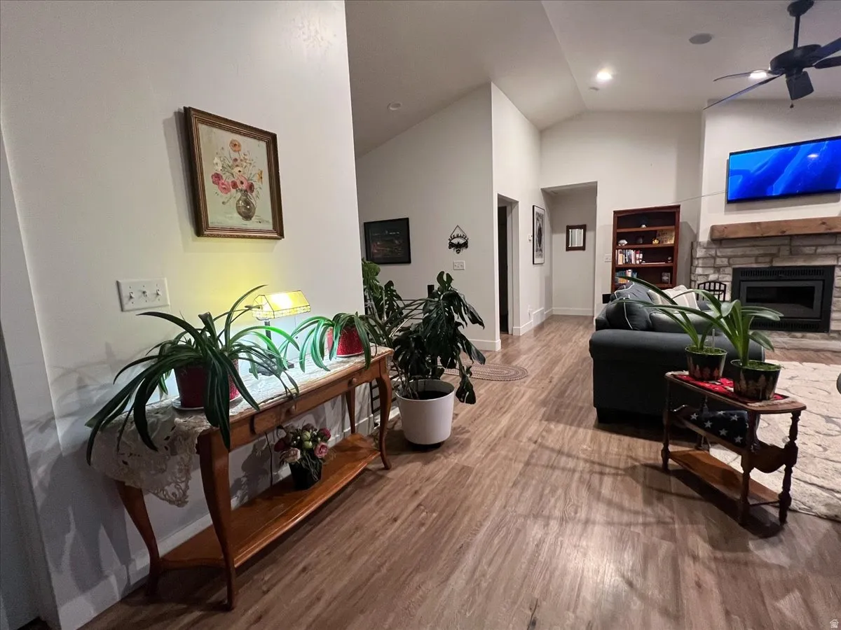 Living room with ceiling fan, lofted ceiling, wood finished floors, and a stone fireplace