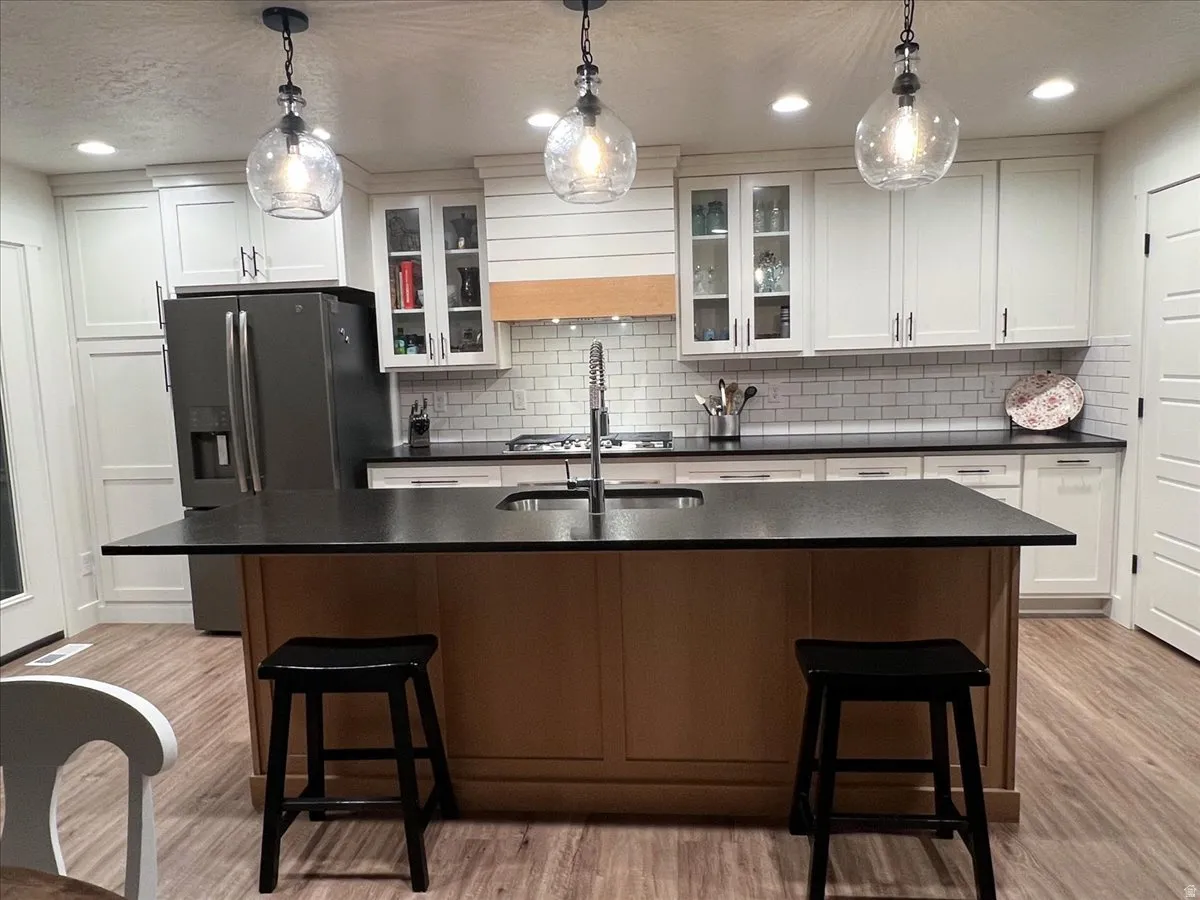 Kitchen with a breakfast bar, glass fronted cabinets, white cabinetry, a kitchen island with sink, and a textured ceiling