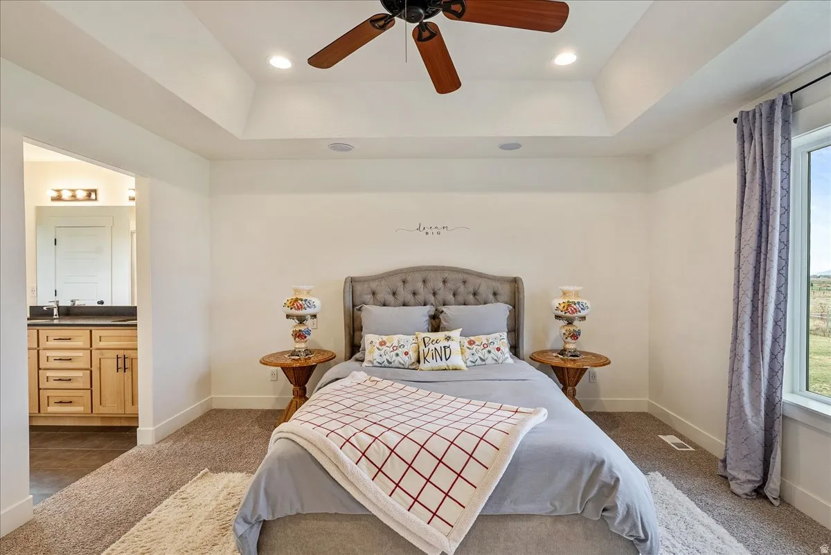 Carpeted bedroom with a raised ceiling, a ceiling fan, ensuite bathroom, and recessed lighting
