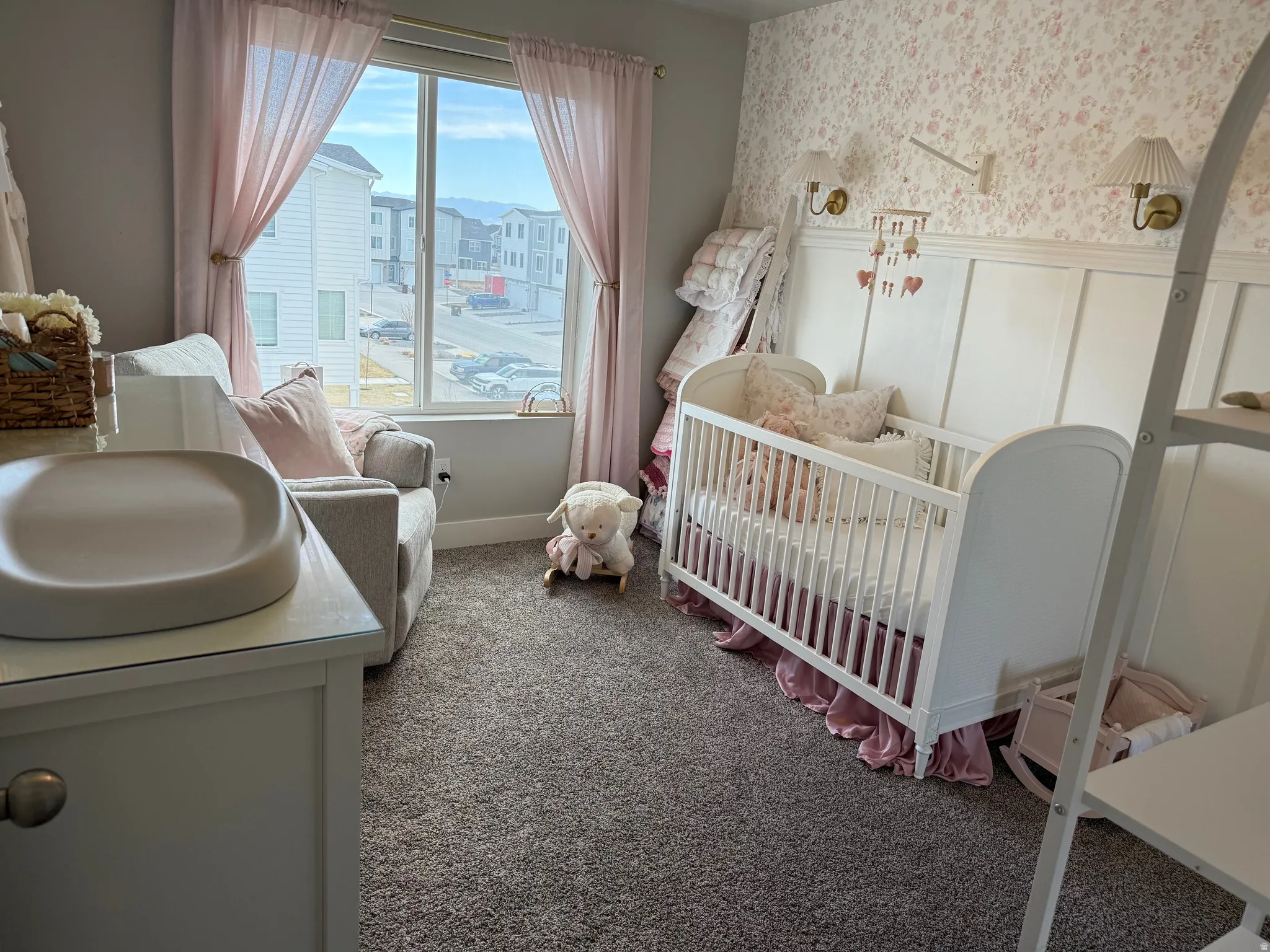 Bedroom with wallpapered walls, a crib, dark carpet, a decorative wall, and wainscoting