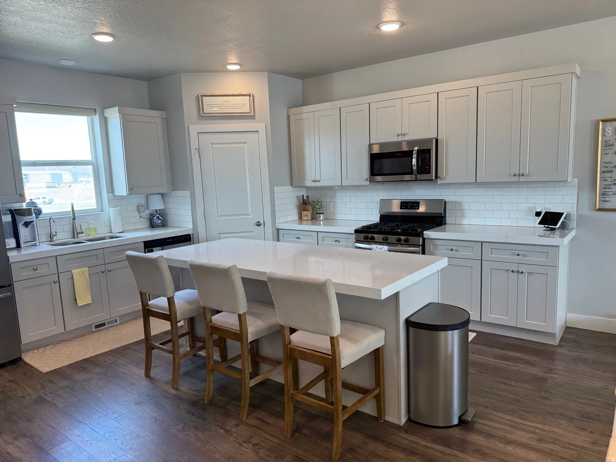 Kitchen with stainless steel appliances, dark wood finished floors, a kitchen island, a kitchen breakfast bar, and white cabinets, gas range