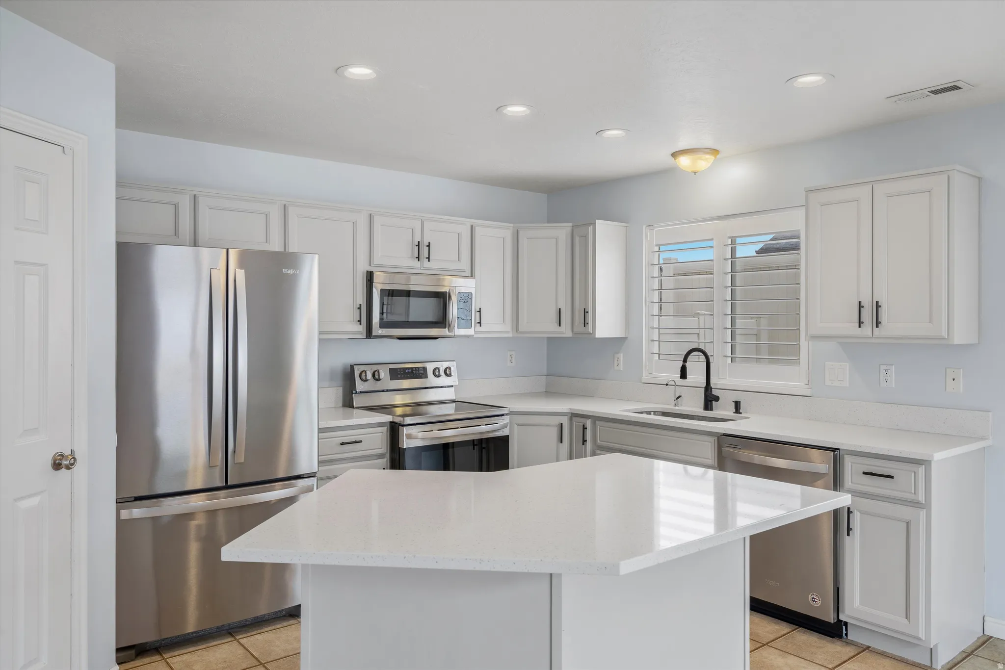 Kitchen with stainless steel appliances, light stone countertops, white cabinetry, recessed lighting, and a center island