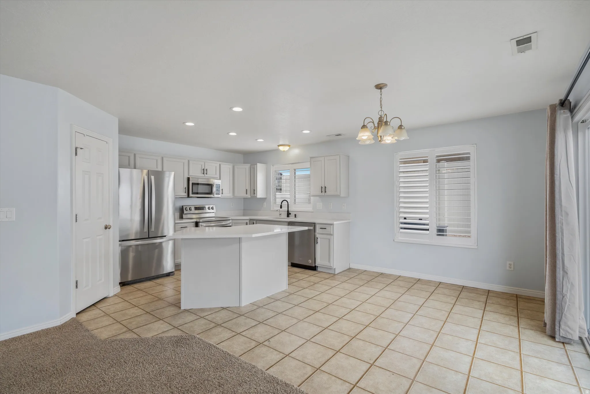 Kitchen featuring light tile patterned floors, stainless steel appliances, a chandelier, a kitchen island, and white cabinets