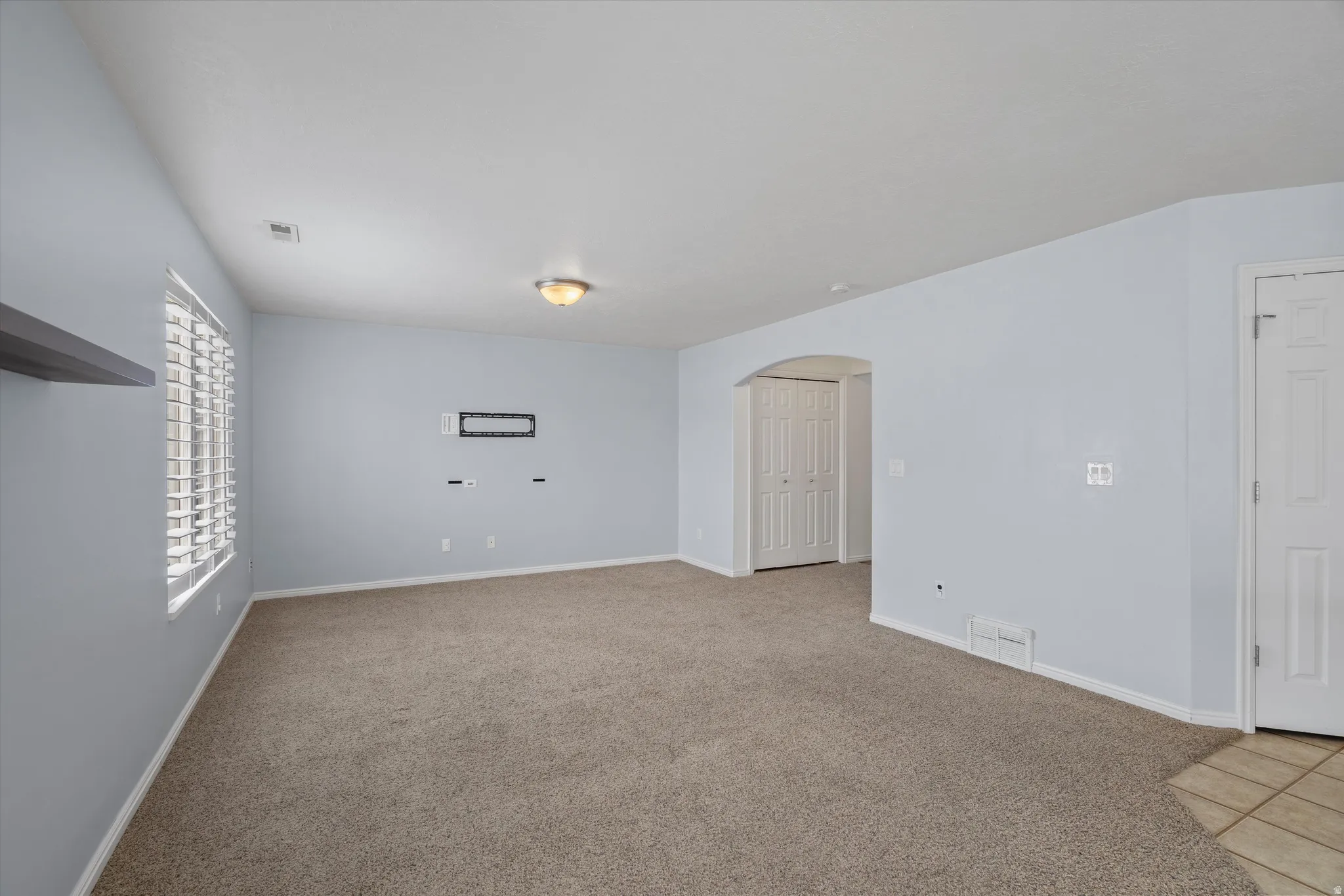 Unfurnished room with arched walkways and light colored carpet