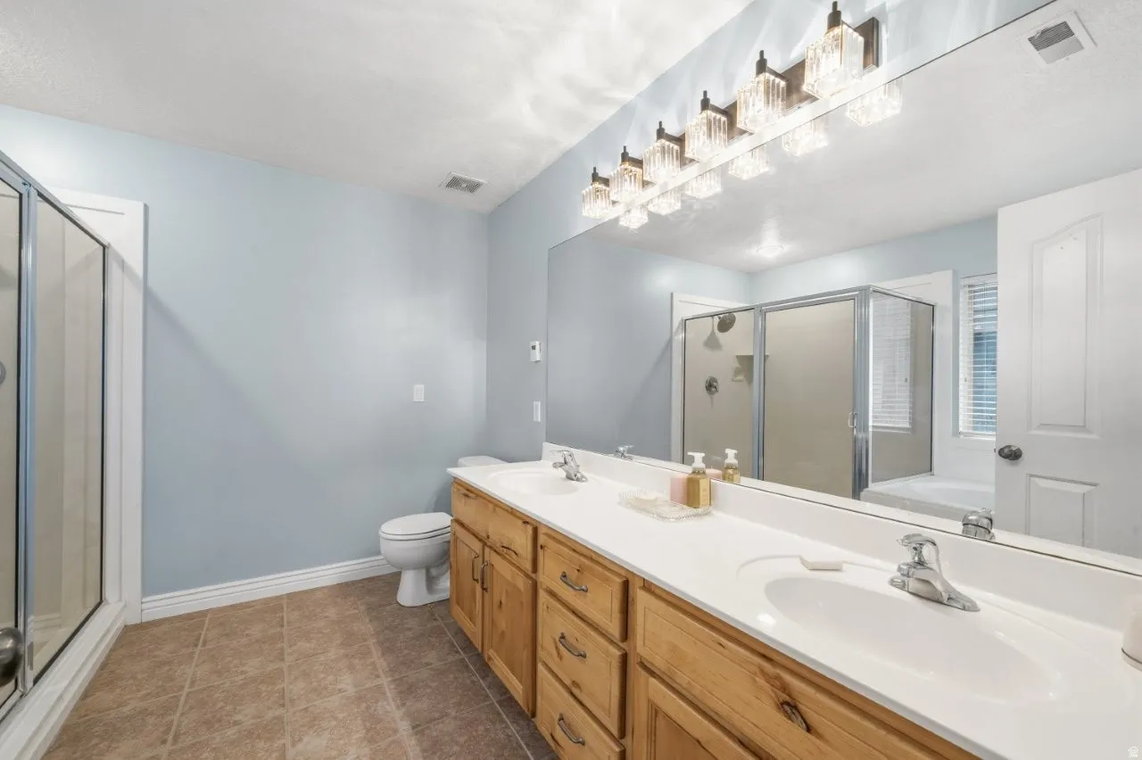 Master Bathroom featuring double vanity, a shower stall, a bath, and dark tile patterned flooring