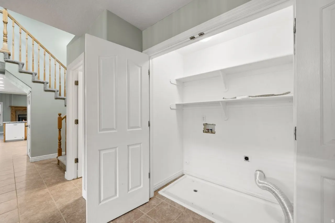Laundry area with washer hookup, light tile patterned floors, hookup for an electric dryer, and a warm lit fireplace