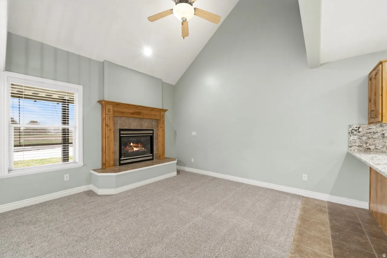 Unfurnished living room featuring vaulted ceiling, ceiling fan, a tile fireplace, and light carpet