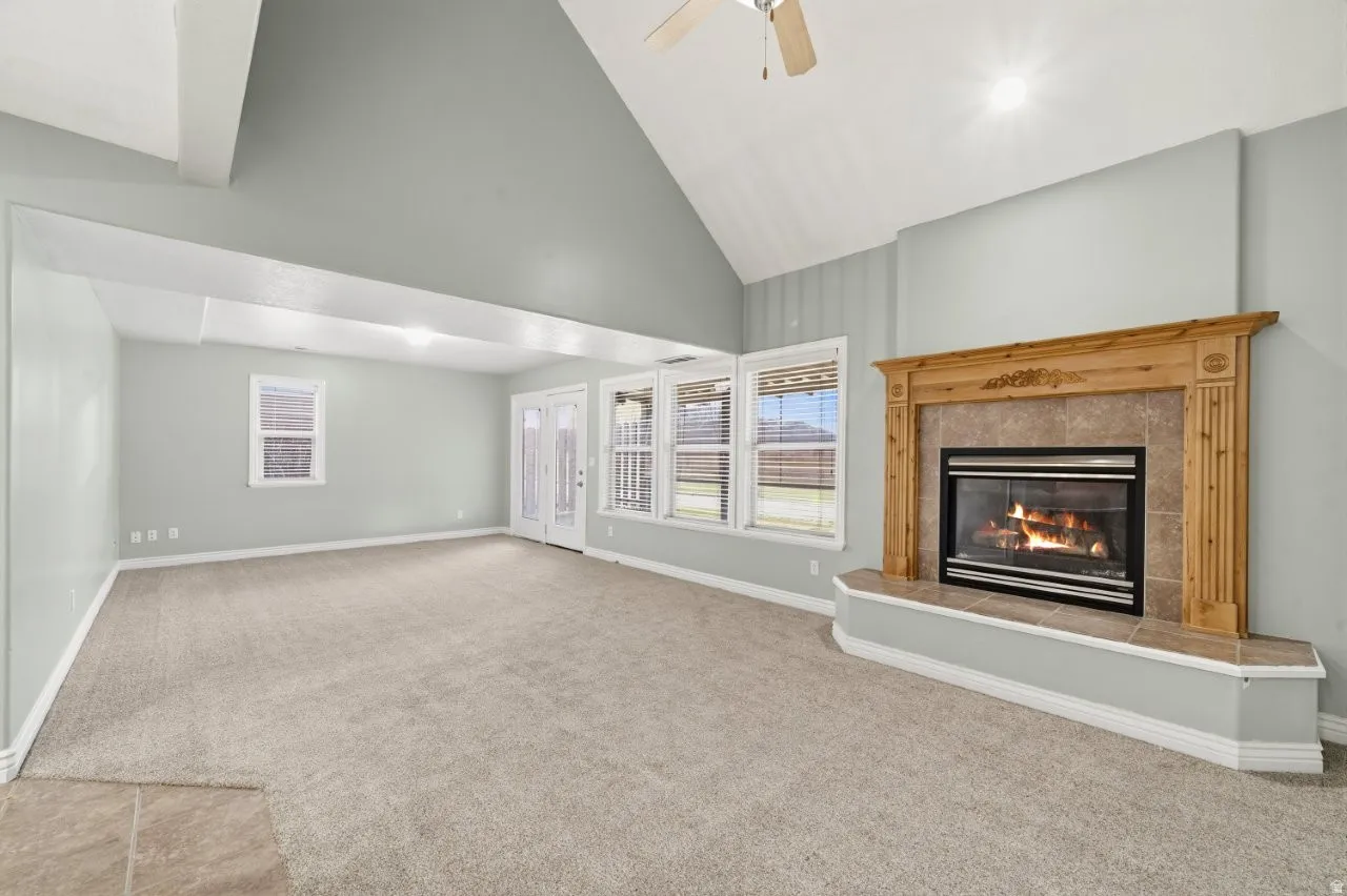 Unfurnished living room featuring carpet, a tiled fireplace, ceiling fan, and vaulted ceiling