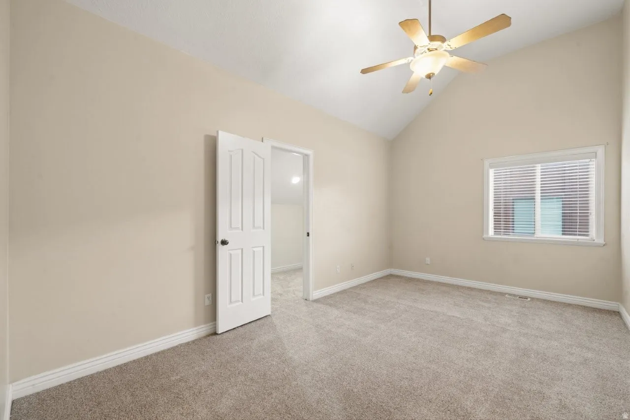 Spare room featuring light colored carpet, lofted ceiling, and ceiling fan