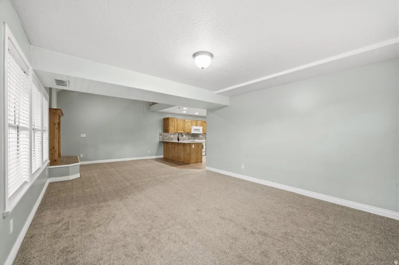 Unfurnished living room featuring light carpet, bar with sink, and a textured ceiling
