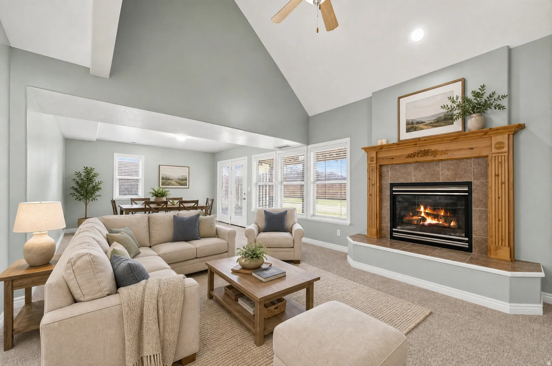 Vaulted ceiling living area featuring a central fireplace with a wood mantel and tile surround, multiple windows, and light-colored carpeting