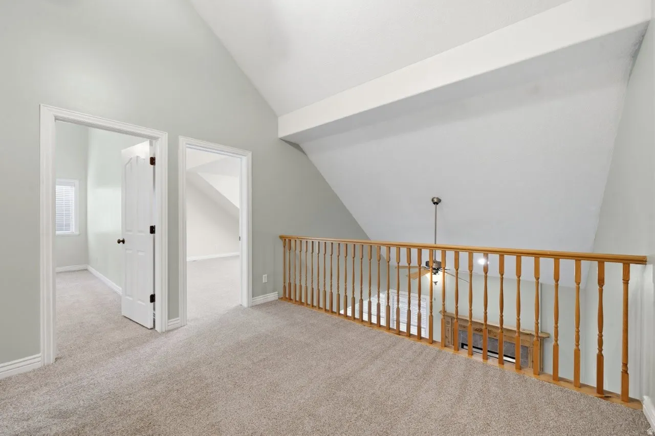 Hallway featuring vaulted ceiling and light colored carpet