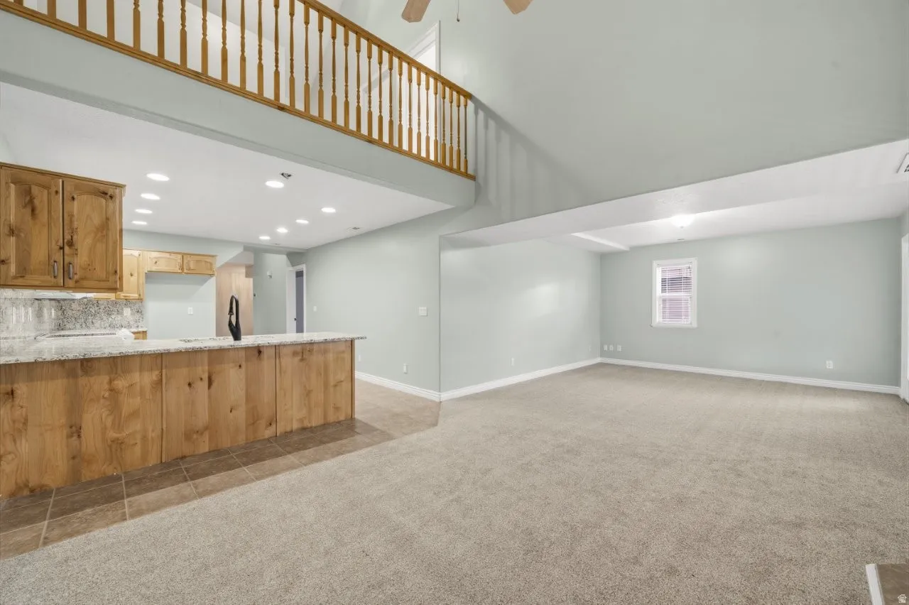 Unfurnished living room featuring a high ceiling, recessed lighting, light colored carpet, and a ceiling fan