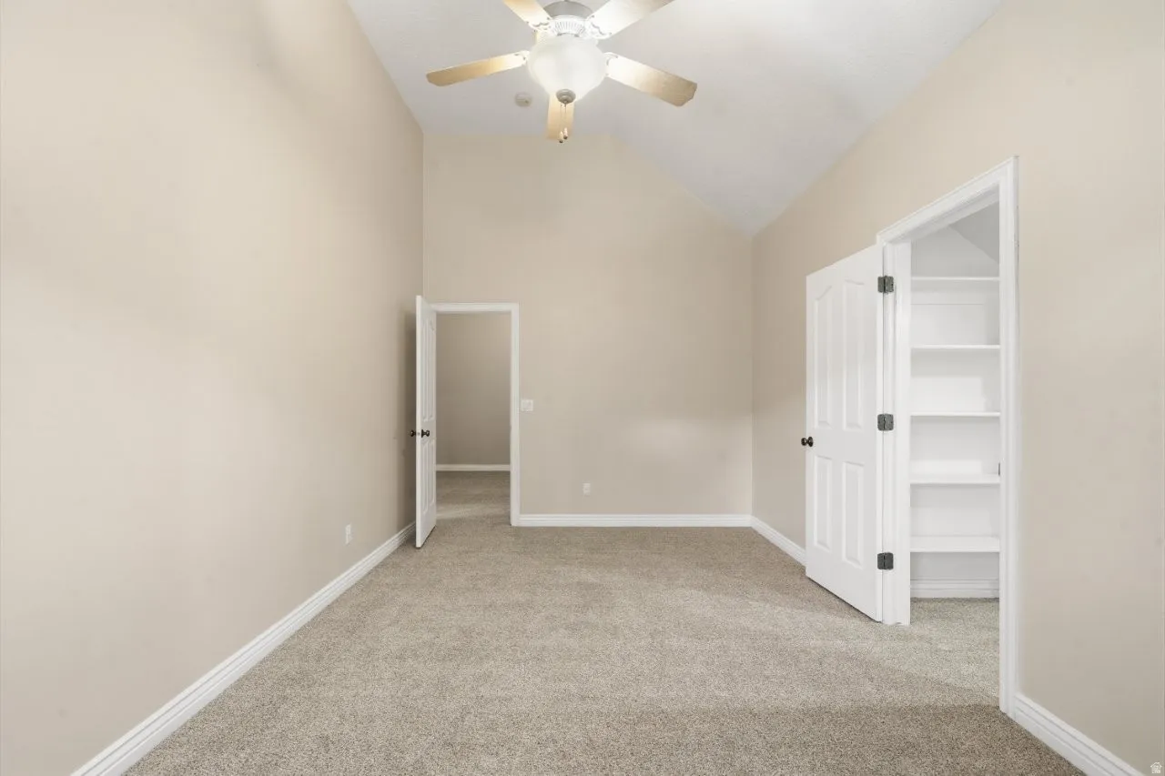Spare room with light carpet, vaulted ceiling, and a ceiling fan