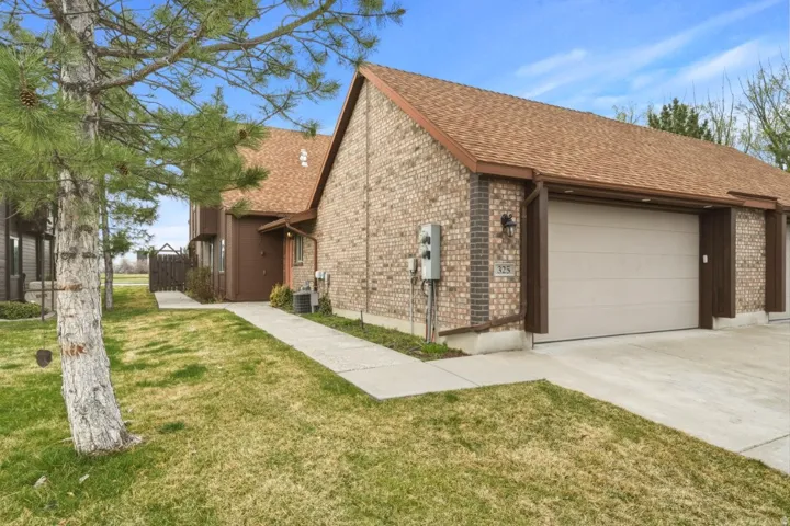 View of side of home featuring brick siding, a shingled roof, a garage, driveway, and a lawn