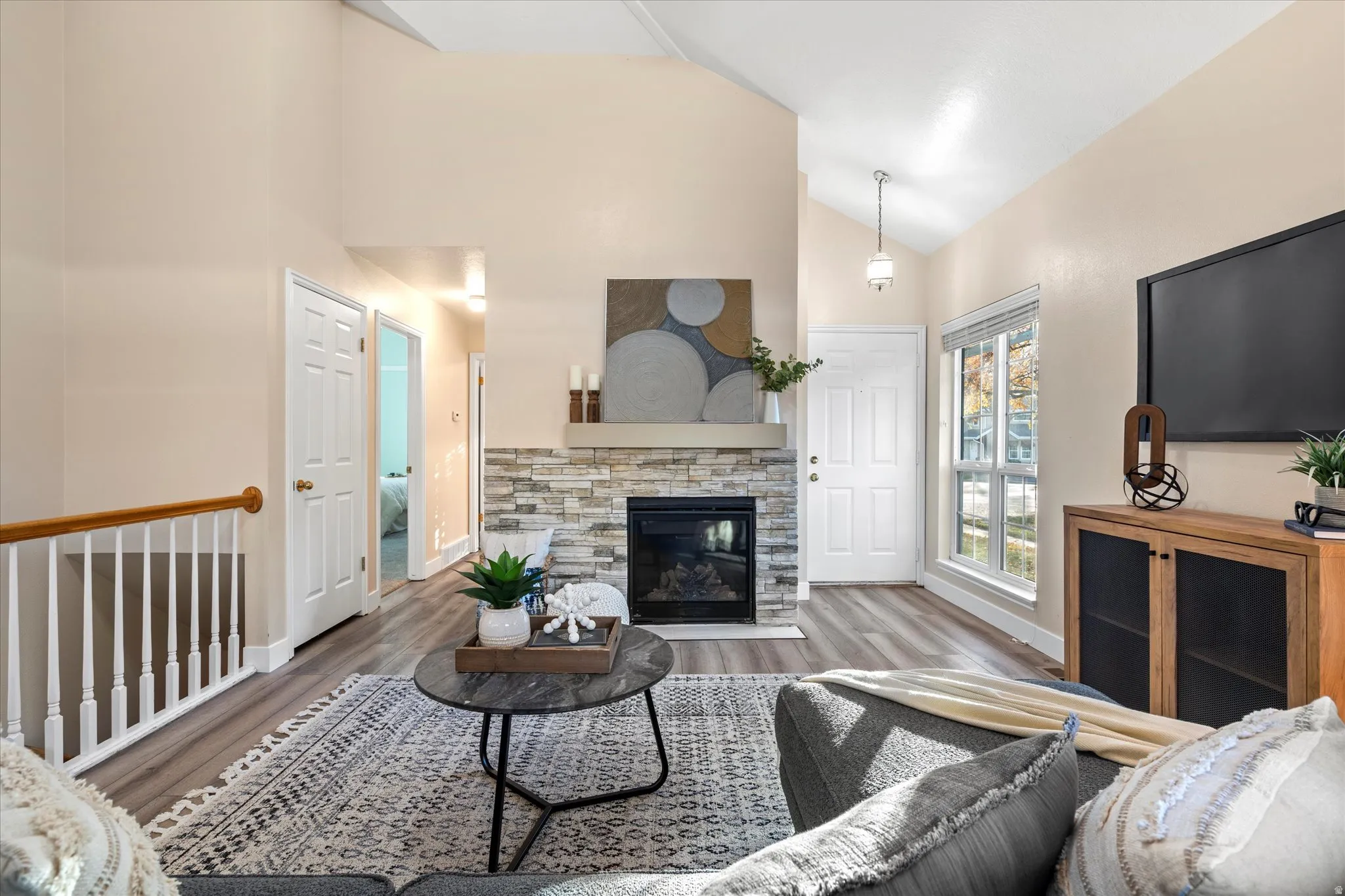 Living area with wood finished floors, lofted ceiling, and a stone fireplace