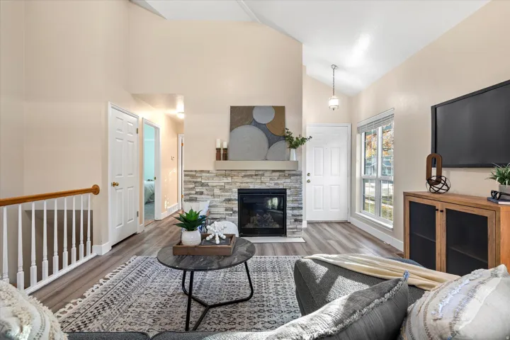 Living area with wood finished floors, lofted ceiling, and a stone fireplace