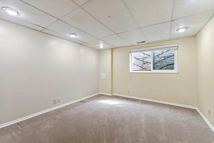 Spacious lower-level bedroom with neutral tones, soft carpeting, and recessed lighting, offering comfortable and flexible use.