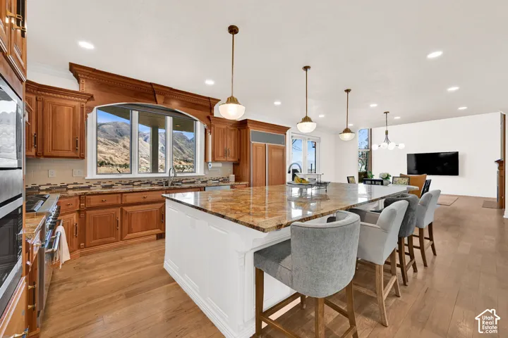 Kitchen featuring dark stone countertops, backsplash, a breakfast bar, light wood-style flooring, and crown molding