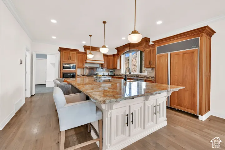 Kitchen featuring a kitchen breakfast bar, light stone countertops, built in appliances, a large island with sink, and crown molding