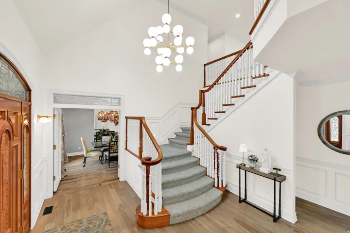 Entrance foyer with suspended lighting, a decorative wall, ornamental molding, wainscoting, and light wood finished floors