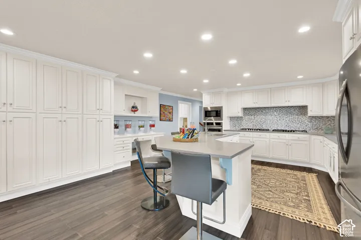 Kitchen with a breakfast bar, crown molding, white cabinetry, an island with sink, and stainless steel appliances