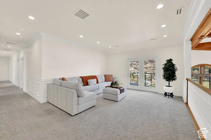 Living room with a wainscoted wall, crown molding, a decorative wall, light carpet, and recessed lighting